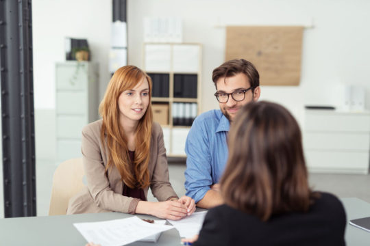 40290917 - investment broker meeting with a young couple in her office to discuss their financial needs, view from behind the agent of the couple